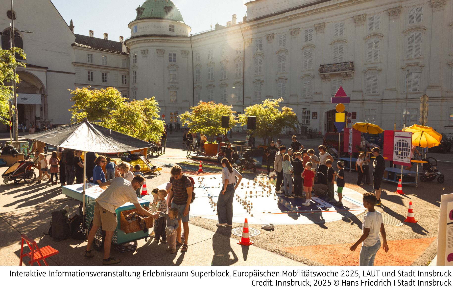 Foto von Personen in Innsbruck, die miteinander in Gruppen reden, einige Kinder. Mitmachstation.