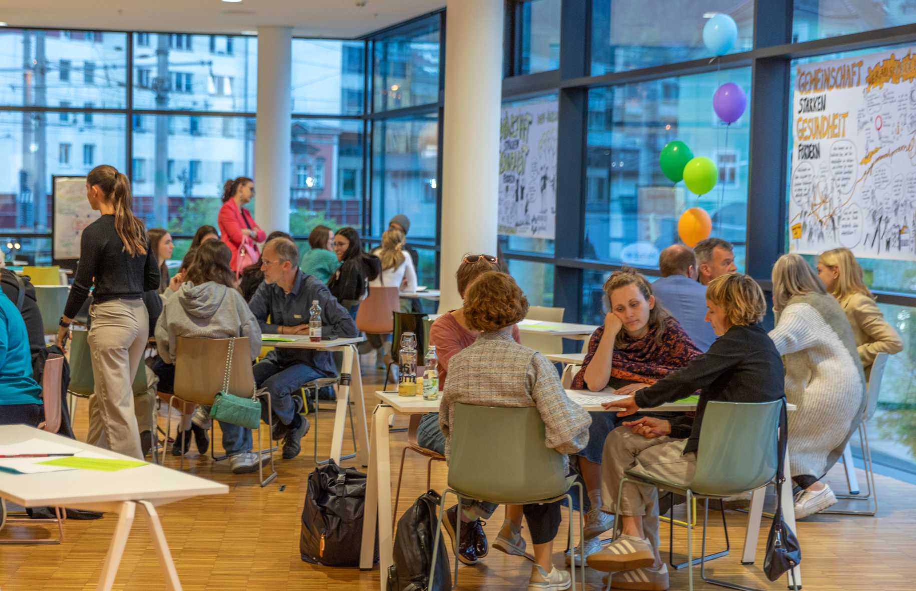 Menschen sitzen beim Stadtforum in einem Raum an Gruppentischen zusammen.